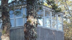 Puinen mökki, jossa on suuri ikkuna ja parveke, ja sen ympärillä on paljon puita.