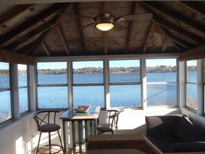 A rustic cabin with a dining area, a ceiling fan, and a view of a lake.