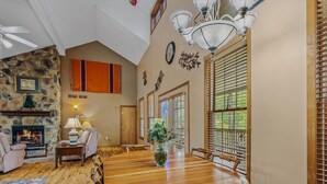 A spacious dining area with a large wooden table, surrounded by chairs, and a stone fireplace. - Blue Badger Cottage-wifi, screen porch, fire pit, game room, king bed, fireplace (Berkeley Springs)