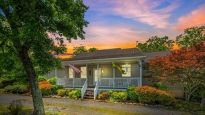 A two-story house with a front porch, a small garden, and a tree in the foreground. - Blue Badger Cottage-wifi, screen porch, fire pit, game room, king bed, fireplace (Berkeley Springs)