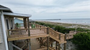 Une terrasse en bois à plusieurs niveaux, dotée de mobilier d’extérieur, qui offre une vue sur une plage et une jetée.