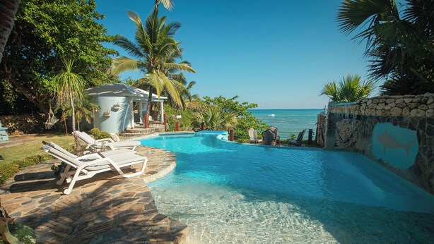 A clear blue pool with lounge chairs, a stone wall, and a view of the ocean.