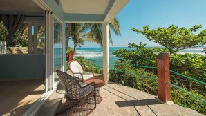 A balcony with a view of the ocean, a chair, and a table.
