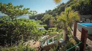 A lush garden with a pool, a stone wall, and a view of the ocean.