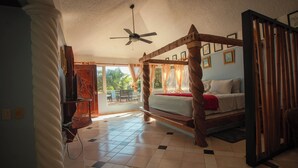 A bedroom with a wooden four-poster bed, a ceiling fan, and a view of the outdoors.