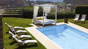 Ein Poolbereich mit Liege und Liegestühlen, mit Blick auf eine schöne Landschaft aus Meer und Hügeln.