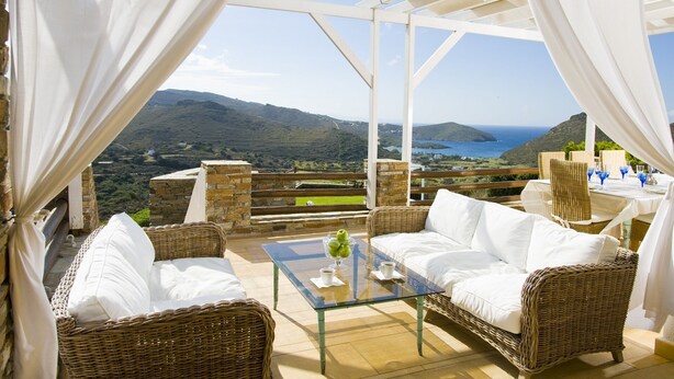 Eine Terrasse mit Korbmöbeln, einem Glastisch und Blick auf das Meer und die Hügel.