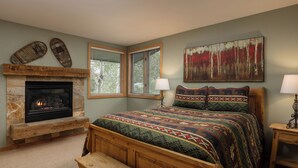 Ein Schlafzimmer mit Kamin aus Stein, einem Bett mit gemusterten Betttextilien und einem Baumgemälde.