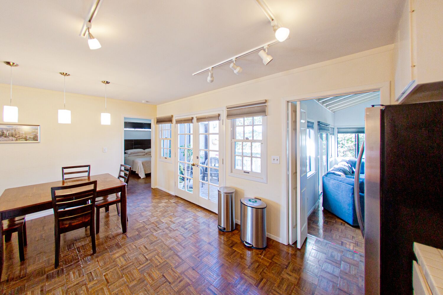 A spacious room with a wooden floor, a dining table with chairs, a bed, and a window.