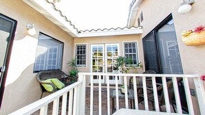 Ein überdachter Patio-Bereich mit Korbmöbeln, Topfpflanzen und einem weißen Geländer.