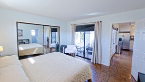 Ein Hotelzimmer mit einem großen Bett, einem Spiegel, einem Balkon mit Sitzgelegenheiten und einer Küchenzeile.