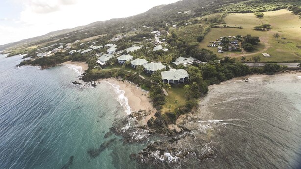 An aerial view of a coastal resort with multiple buildings, a beach, and rocky shoreline.