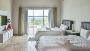 A hotel room with two beds, a TV, a desk, and a view of the sea.