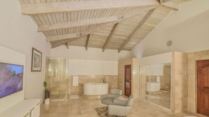 A spacious bedroom with a large bed, a seating area with a chair, a television, and a bathroom with a bathtub and shower.