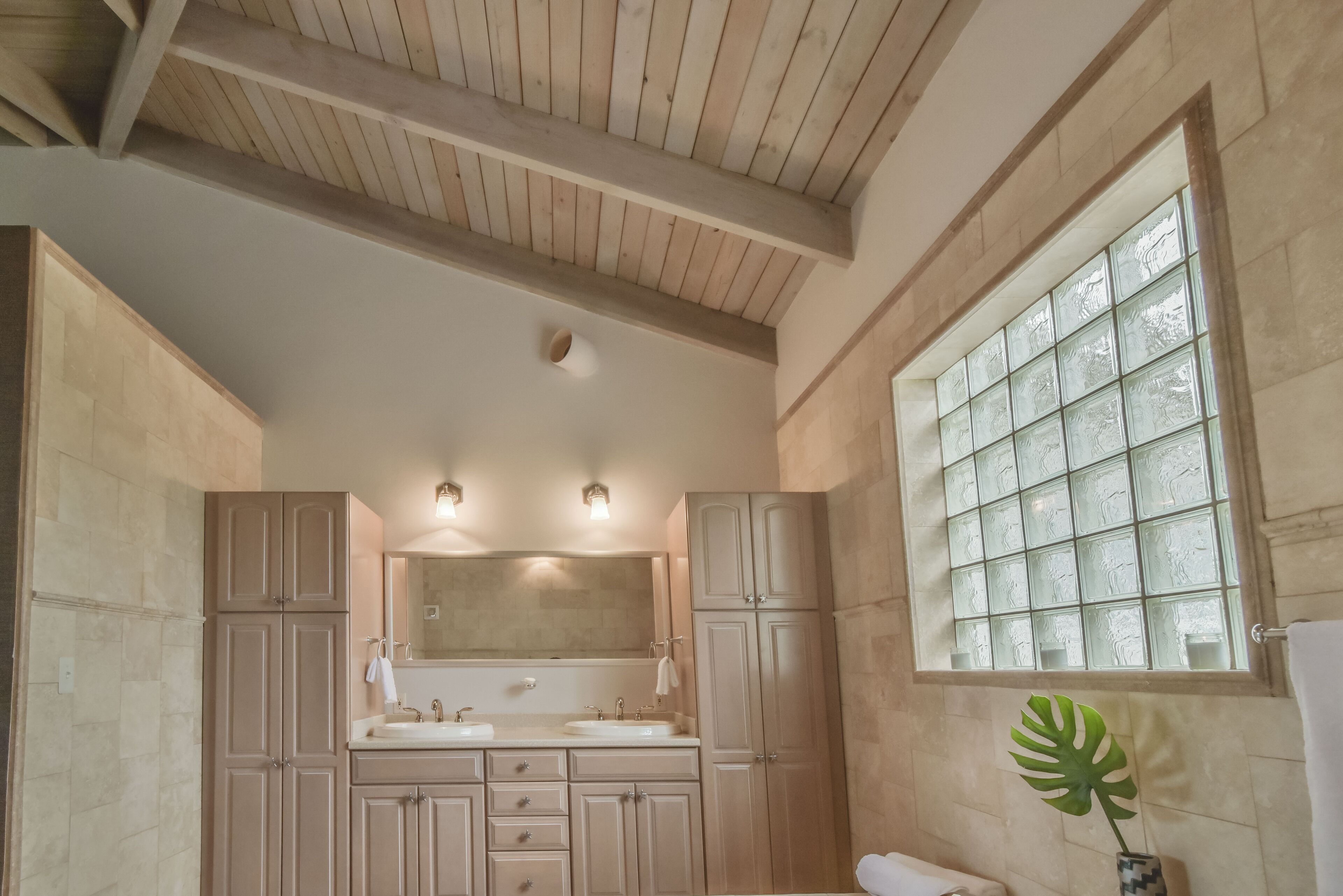 Ein Badezimmer mit Holzboden, einem großen Spiegel, zwei Waschbecken und einem Fenster mit Milchglas.