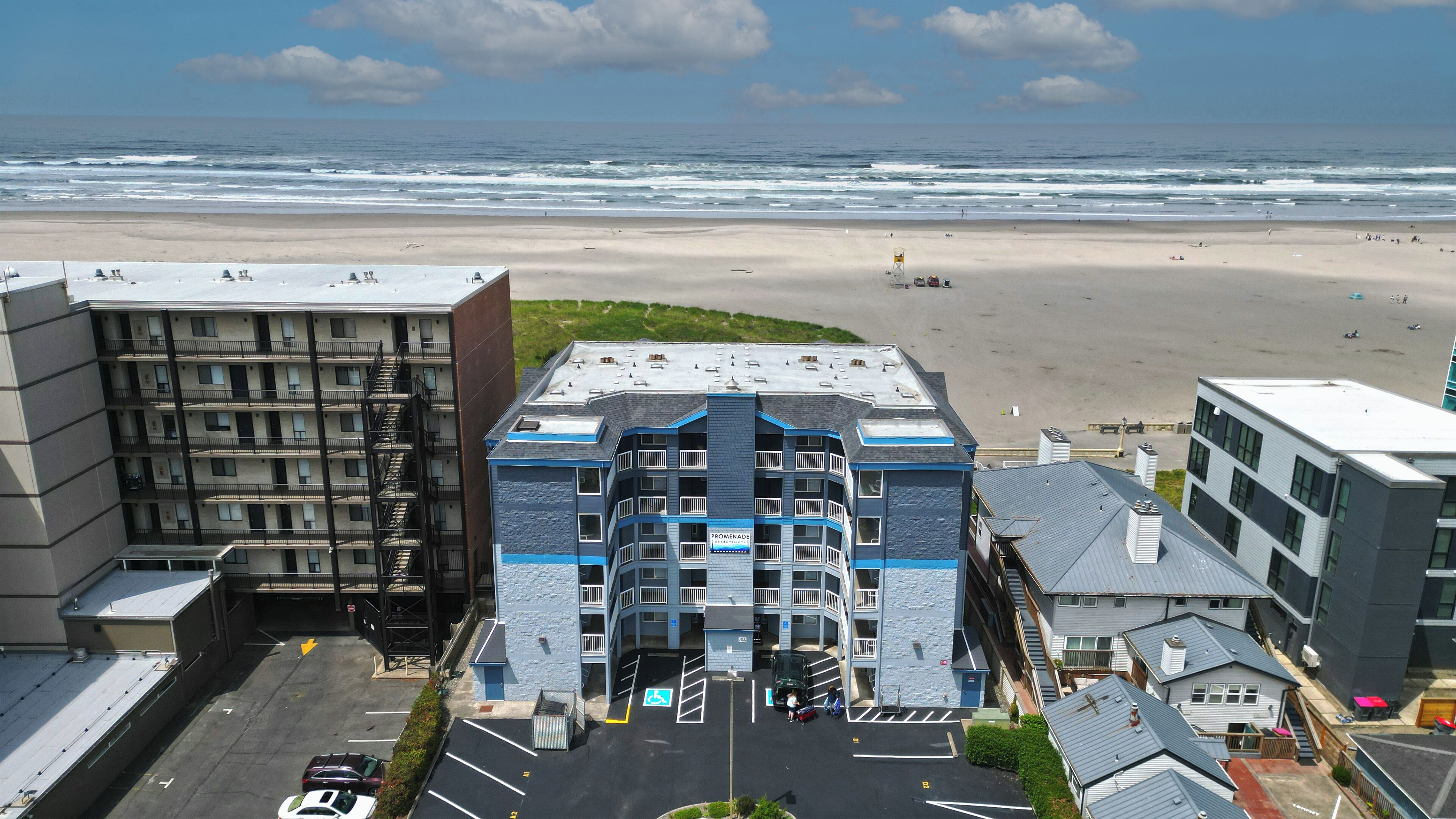 Un immeuble à plusieurs étages, avec un parking à l’avant, donnant sur une plage.