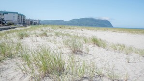 Een zandstrand met duinen en een gebouw op de achtergrond.