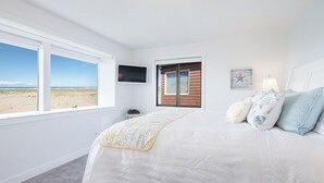 Een slaapkamer met een groot bed, een televisie, een raam met uitzicht op het strand en een deur naar buiten.