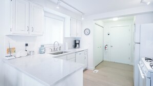Een moderne keuken met witte kasten, een centraal eiland, een ingebouwde oven en een koffiezetapparaat.