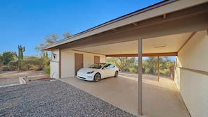 A white car parked in a covered garage with a desert landscape in the background. - Old Western Sonoran Desert Getaway (Cave Creek)