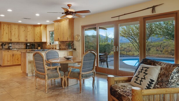 A spacious kitchen with wooden cabinets, a dining area with two chairs, and a view of a swimming pool through large sliding glass doors. - Old Western Sonoran Desert Getaway (Cave Creek)
