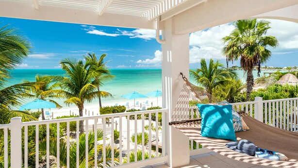 A balcony with a hammock, a view of the beach, and a clear blue sky.