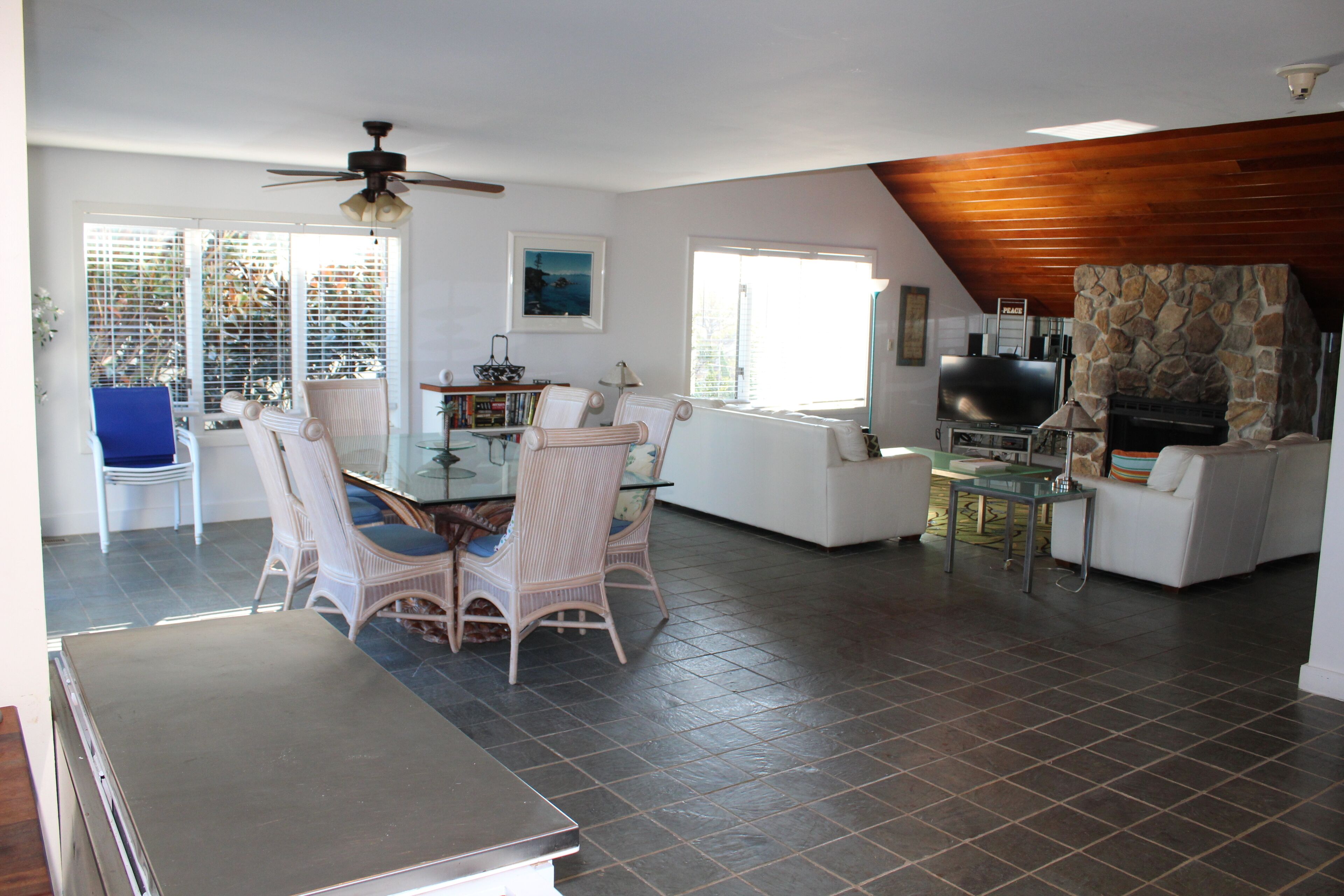 A spacious living area with a dining table, chairs, a television, and a stone fireplace.