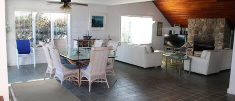 A spacious living area with a dining table, chairs, a television, and a stone fireplace.