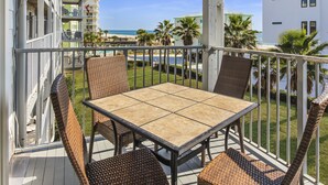 A balcony with wicker chairs and a table, overlooking a beach and palm trees. - Spacious Beachside Condo (Orange Beach)