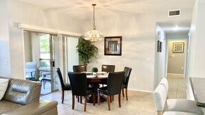 A dining area with a table set for six, surrounded by chairs, a chandelier, and a potted plant.