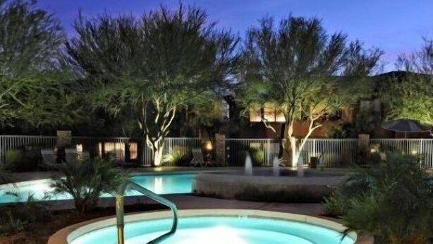 A swimming pool with a curved edge, surrounded by trees and a fence.
