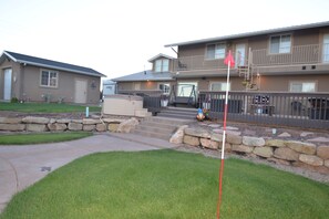 A two-story residential building with a stone retaining wall, a covered patio, and a small front yard. - Tacit Shadow - Single/Queen Sleeps 3 (Parowan)