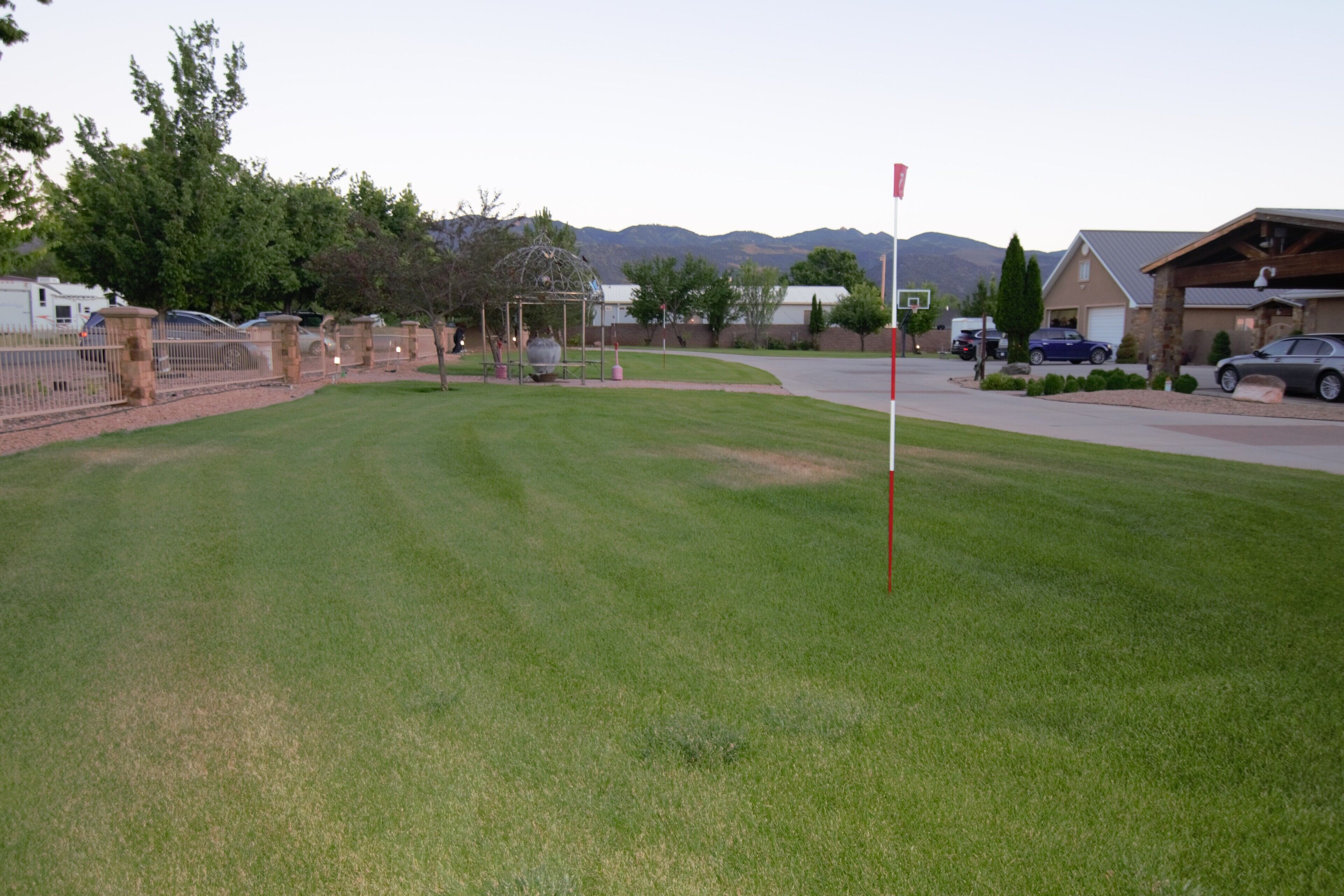 A well-maintained grassy area with a basketball court, a gazebo, and a red flag pole.