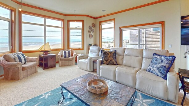 Amplia sala de estar con vista a la playa, que incluye un sofá color beige, dos sillones, una mesa de centro y una lámpara.