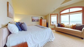 Un dormitorio con una cama grande, un sofá, un armario de madera y vistas al océano.