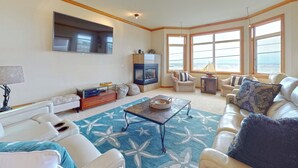 Una sala de estar con chimenea, televisor y vista al mar a través de amplios ventanales.
