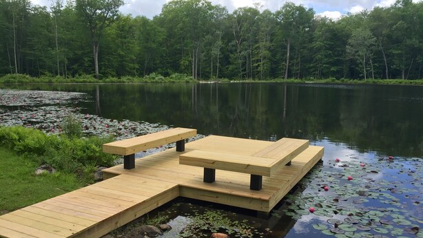 A wooden dock with benches extending into a calm lake surrounded by lush greenery. - Beautiful lake house getaway (Pine Bush)