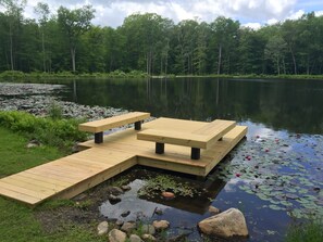 A wooden dock with benches extending into a calm lake surrounded by lush greenery.
