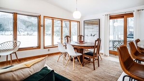 A dining area with a wooden table and chairs, large windows, and a view of a snowy landscape. - Beautiful lake house getaway (Pine Bush)