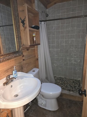 Et badeværelse med vask, toilet, brusebad og et spejl.