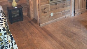 A wooden cabin interior with a bed, a small table with a vase, a mirror, and a door. - Pebble Creek Magical Retreat 2BR 1.5BA Shelter on Stream. Camp/Sleep 10/Linens
 (Laurel Fork)