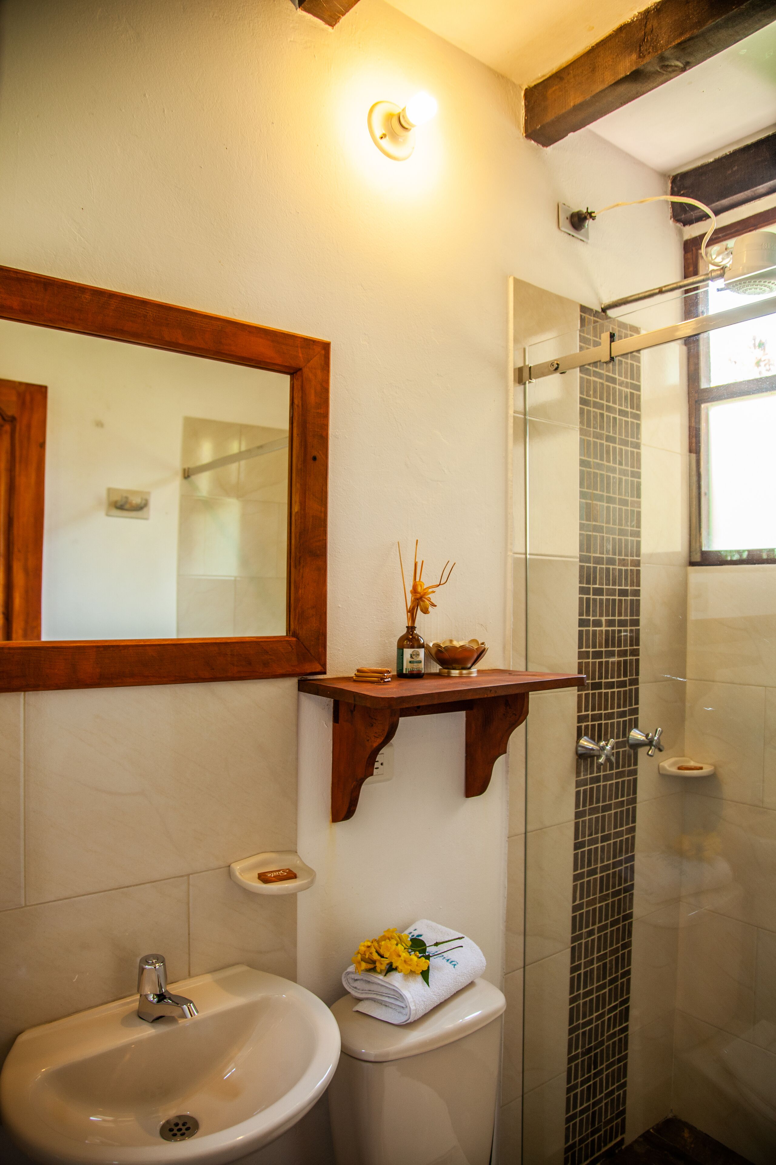 Une salle de bain équipée d’un lavabo, d’un miroir, d’une douche et d’une petite étagère où sont rangés les articles de toilette.
