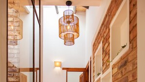 Een trap langs een metselwerkmuur en planken, die leidt naar een badkamer met een wit wastafelmeubel en een hangende lamp.