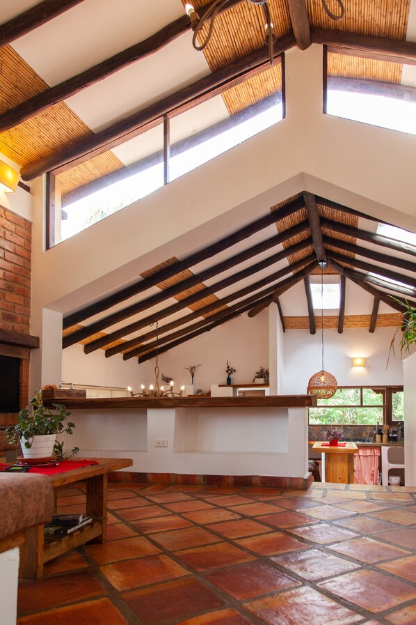 A spacious kitchen with a high ceiling, exposed wooden beams, and large windows allowing natural light.
