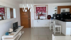 Una sala de estar moderna con televisor, muebles blancos, una puerta de madera y un cuadro.