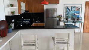 Una cocina moderna con encimera negra, sillas blancas y una lámpara colgante roja.