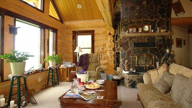 A cozy log cabin interior with a stone fireplace, wooden furniture, and large windows. - Gray's room Garrison Inn Montana bed and breakfast (Kalispell)