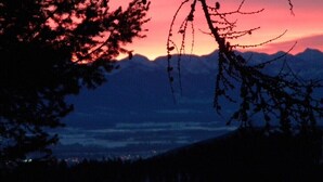 A mountain landscape at dusk with silhouetted trees and a sunset. - Gray's room Garrison Inn Montana bed and breakfast (Kalispell)