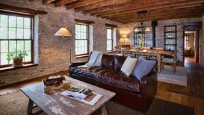 Un interior rústico con vigas de madera a la vista, paredes de piedra, un sofá de cuero, una mesa de comedor y una lámpara.
