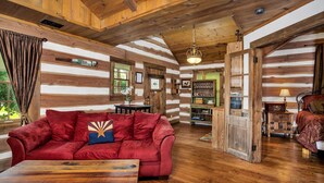 A log cabin interior with a red sofa, wooden flooring, and a rustic ceiling.